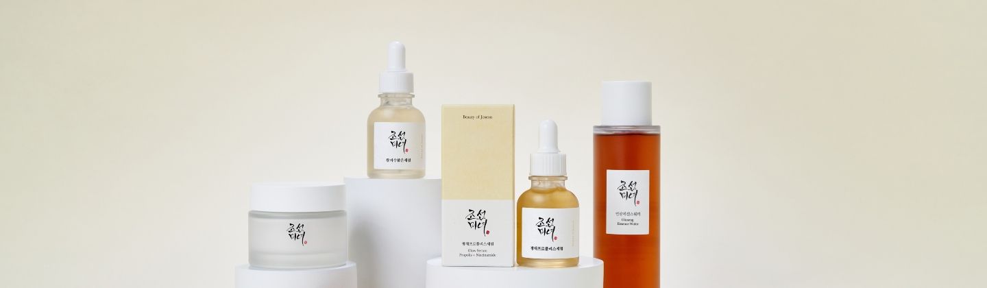 A cream jar, two serum bottles, a toner, and a product box, all part of a Korean skincare line, displayed on white risers.