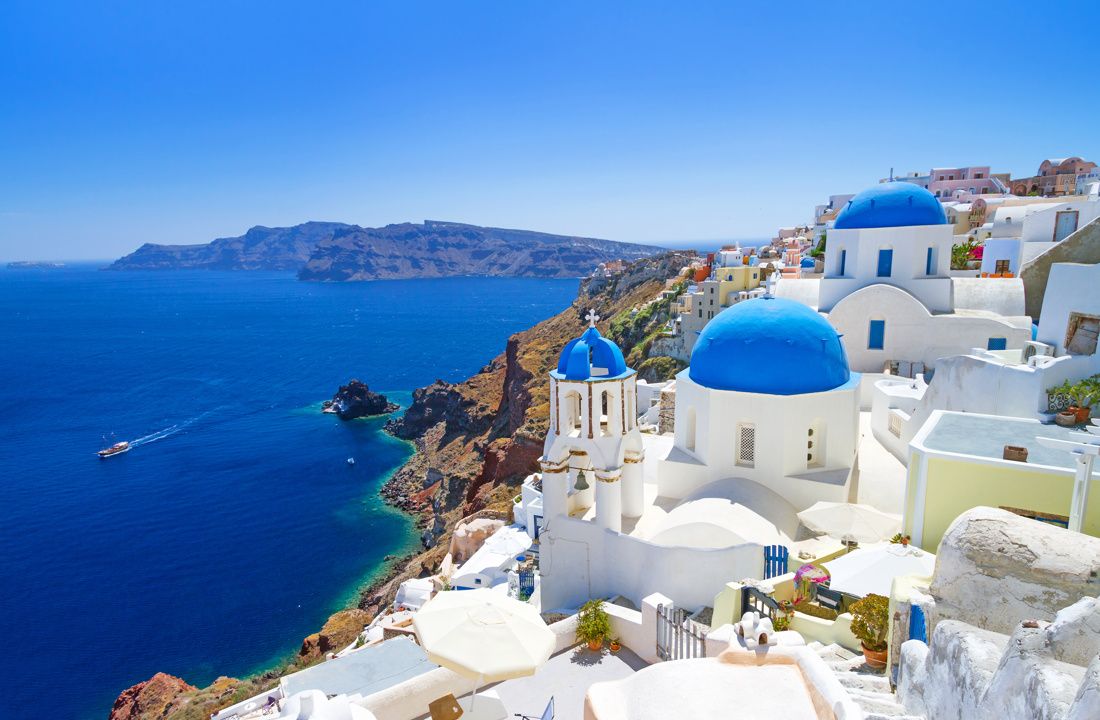 White buildings with blue domes on a cliff overlooking the deep blue sea in Santorini, Greece.