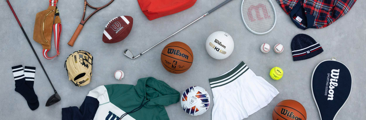 A flat lay of assorted Wilson sports equipment and apparel, including balls, rackets, a golf club, glove, and athletic wear.