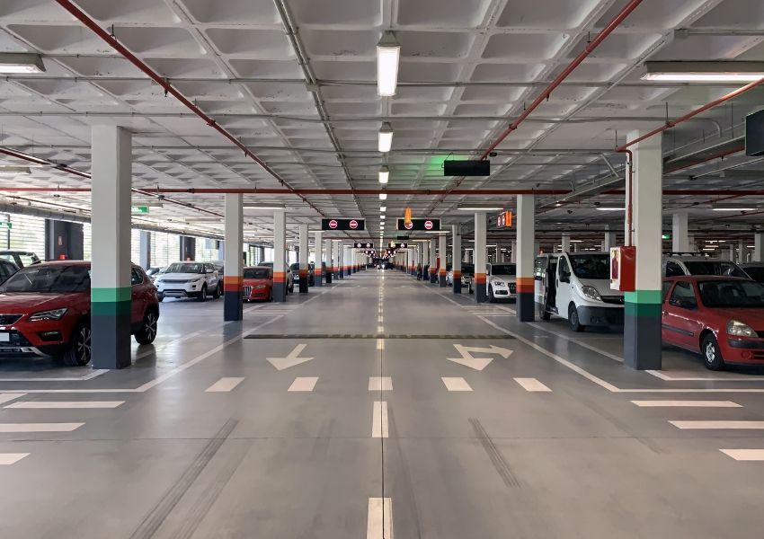 A brightly lit, modern underground parking garage with rows of cars parked.