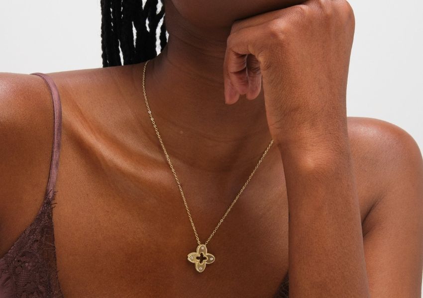 A woman wears a gold clover pendant necklace with clear stones, over a lace camisole.