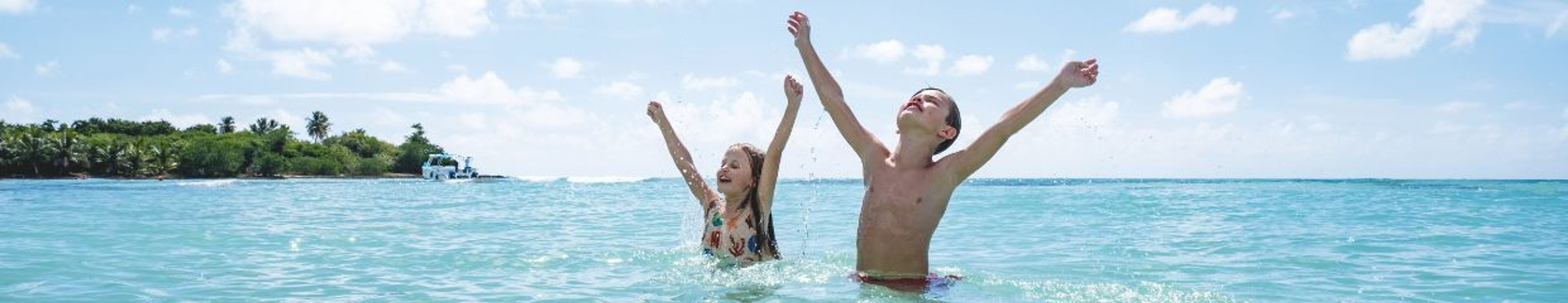 A boy and girl splashing in tropical turquoise ocean water with an island in the background.