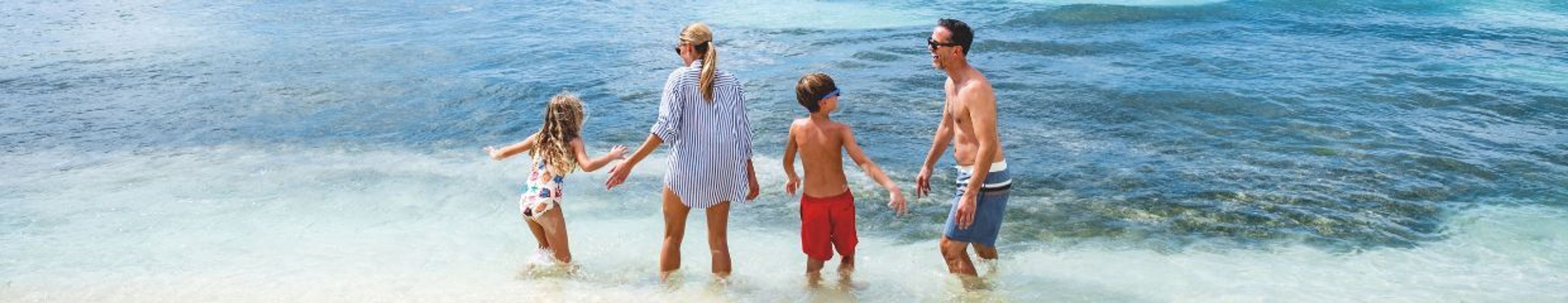 A family of four wading in the shallow ocean water.