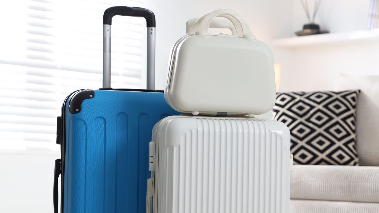 A blue and a white hard-shell suitcase with a small white vanity case stacked on top, indoors.