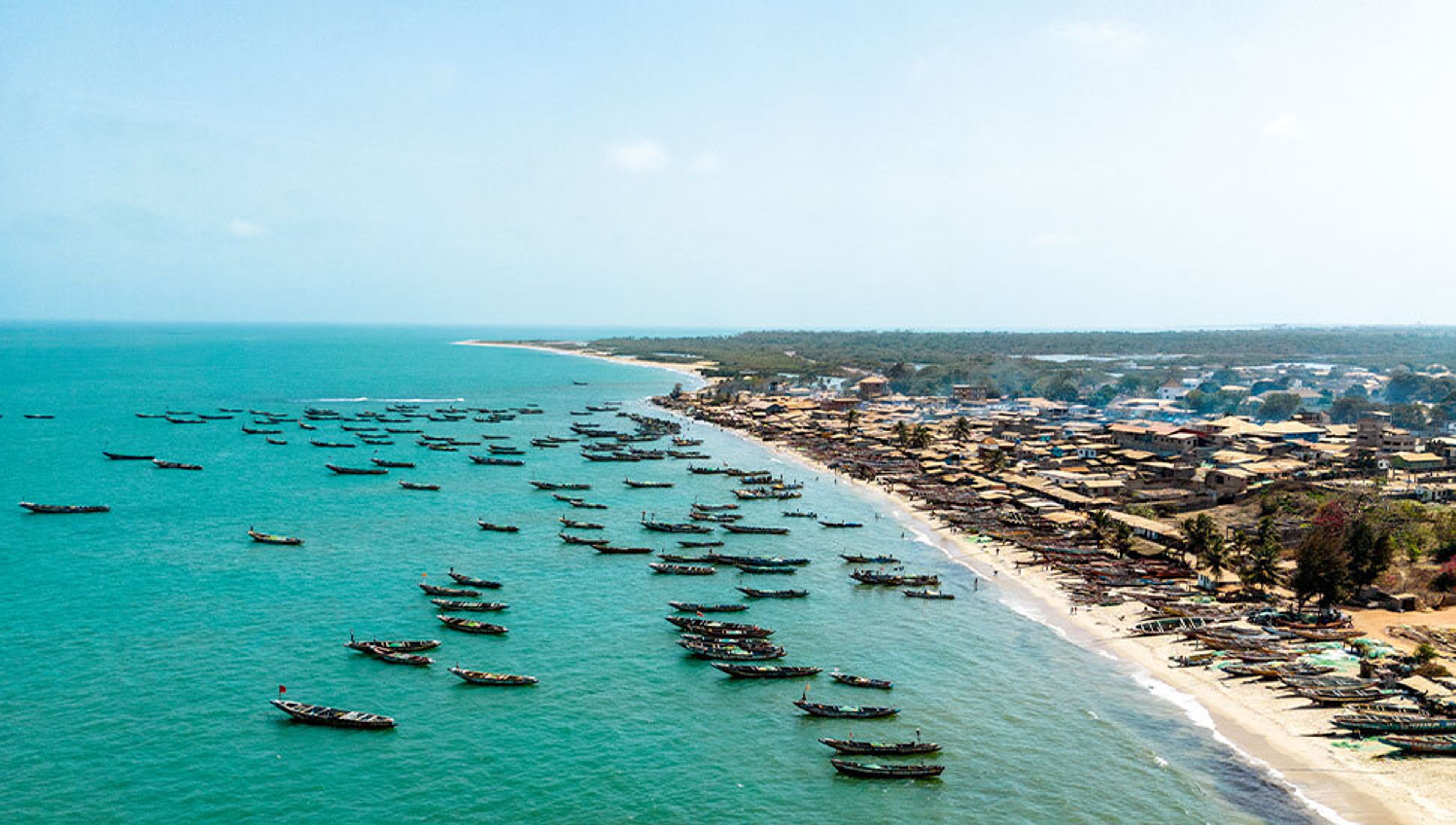 Aerial view of a coastal village with numerous fishing boats in the turquoise sea and on the sandy beach.