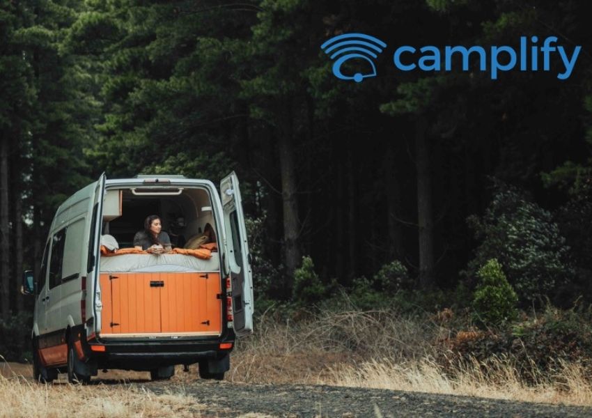 Woman lying in the back of a white camper van in a forest; Camplify logo in the top right.