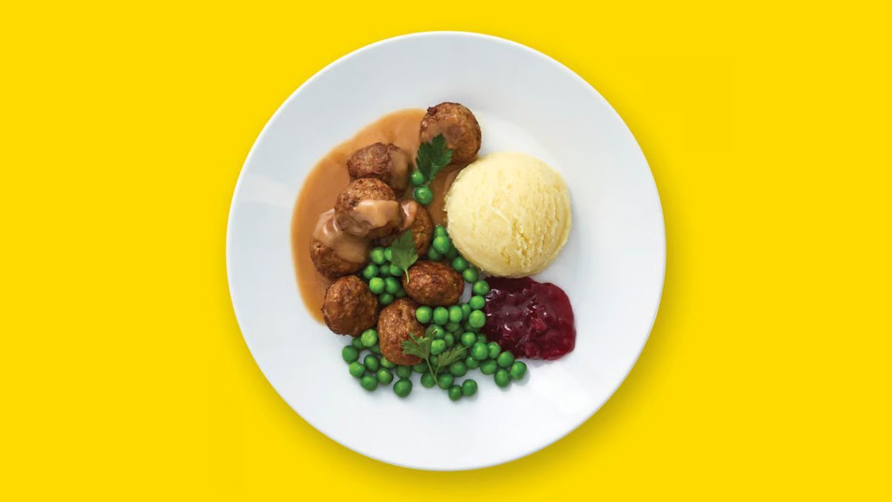 A plate of Swedish meatballs with gravy, mashed potatoes, peas, and lingonberry jam.