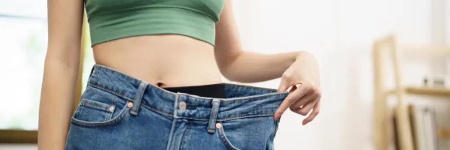 Person's midsection pulling out the waistband of oversized jeans to show weight loss.