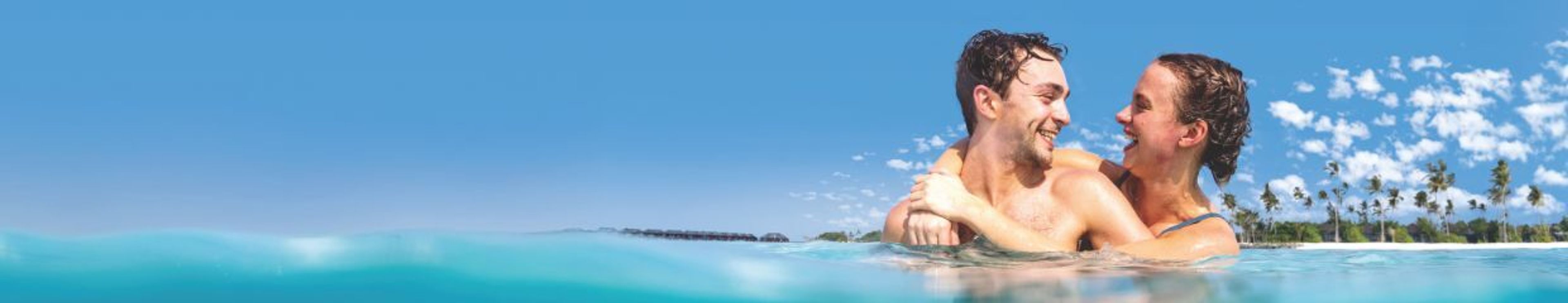 Happy couple embracing in turquoise ocean water with a tropical island in the background.