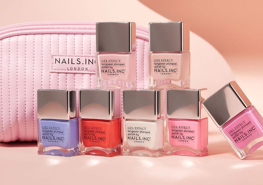 An assortment of Nails.Inc London Gel Effect nail polishes in various bright and pastel shades, next to a pink quilted makeup bag.
