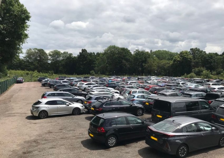 A crowded outdoor parking lot under a cloudy sky, with trees in the background.