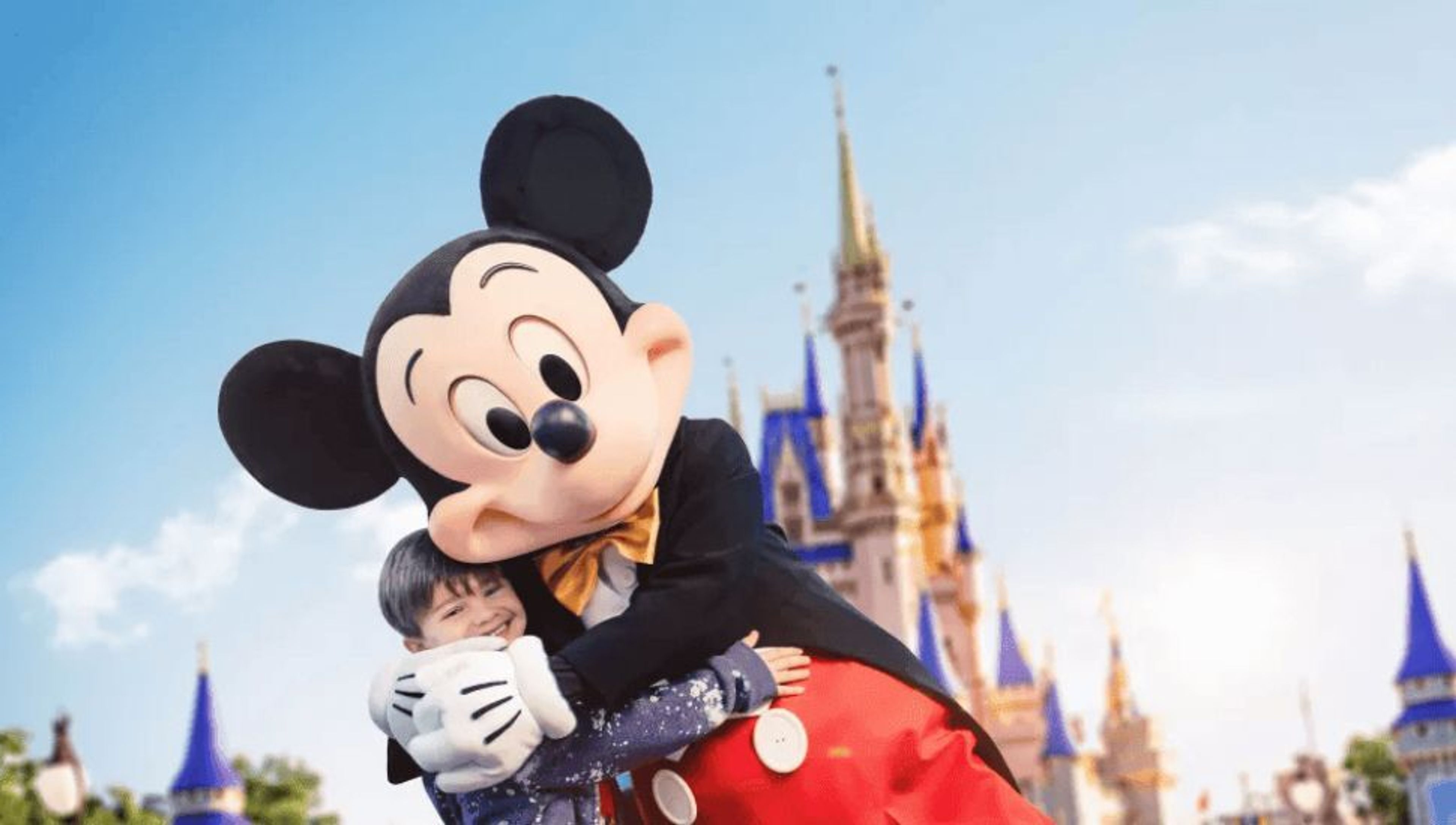 Mickey Mouse hugging a smiling child in front of Cinderella Castle.