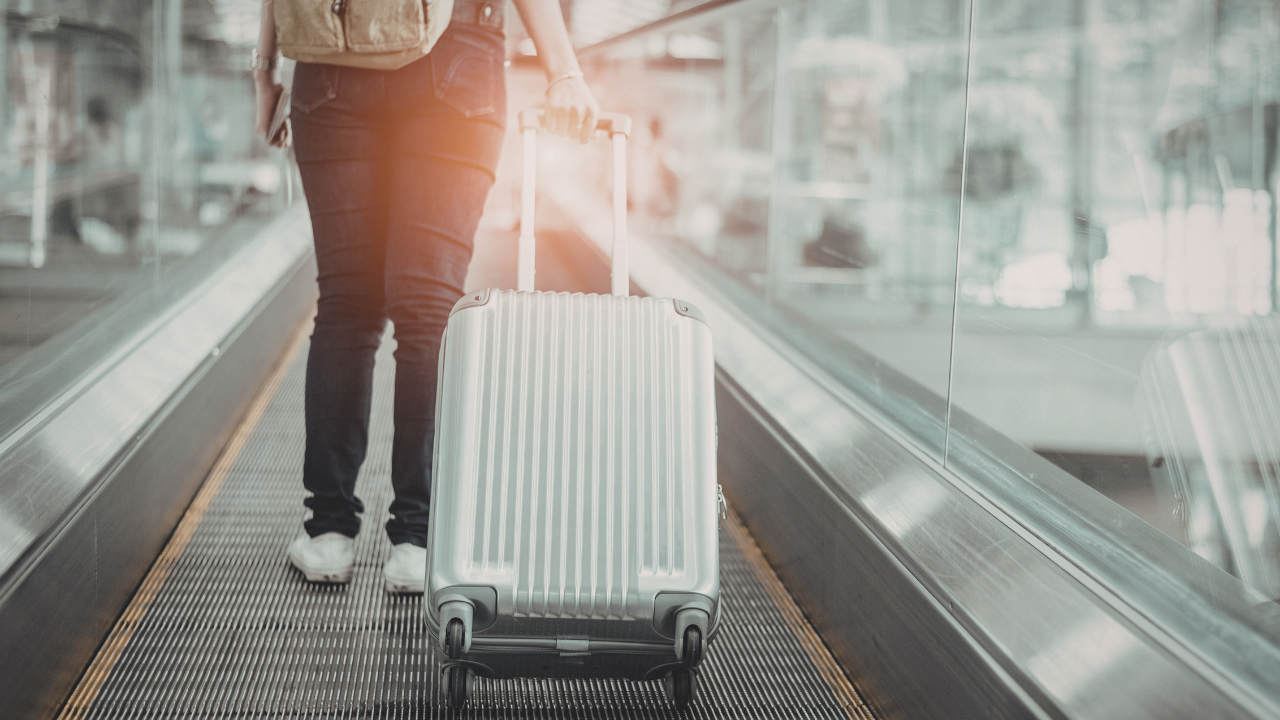 A person pulls a silver rolling suitcase on an airport moving walkway.