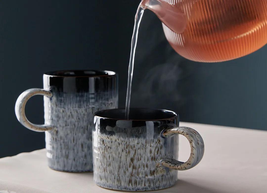 Steaming water is poured into a speckled ceramic mug next to another.