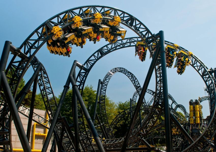 A black roller coaster with yellow cars, some riders upside down, on multiple loops under a blue sky.