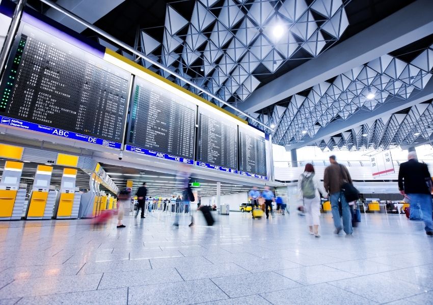 Busy airport terminal with a large flight information board and blurred people walking.