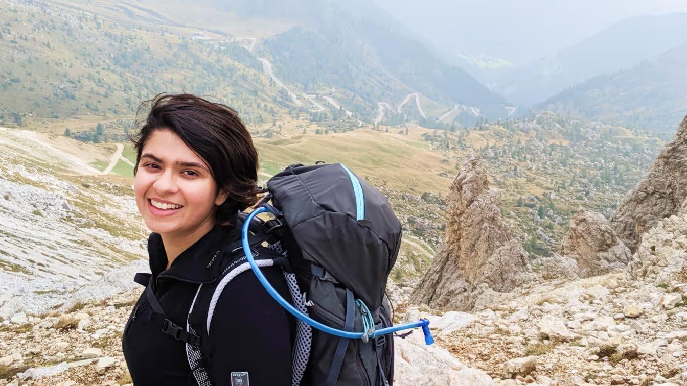 A smiling woman with a backpack in a mountainous landscape.