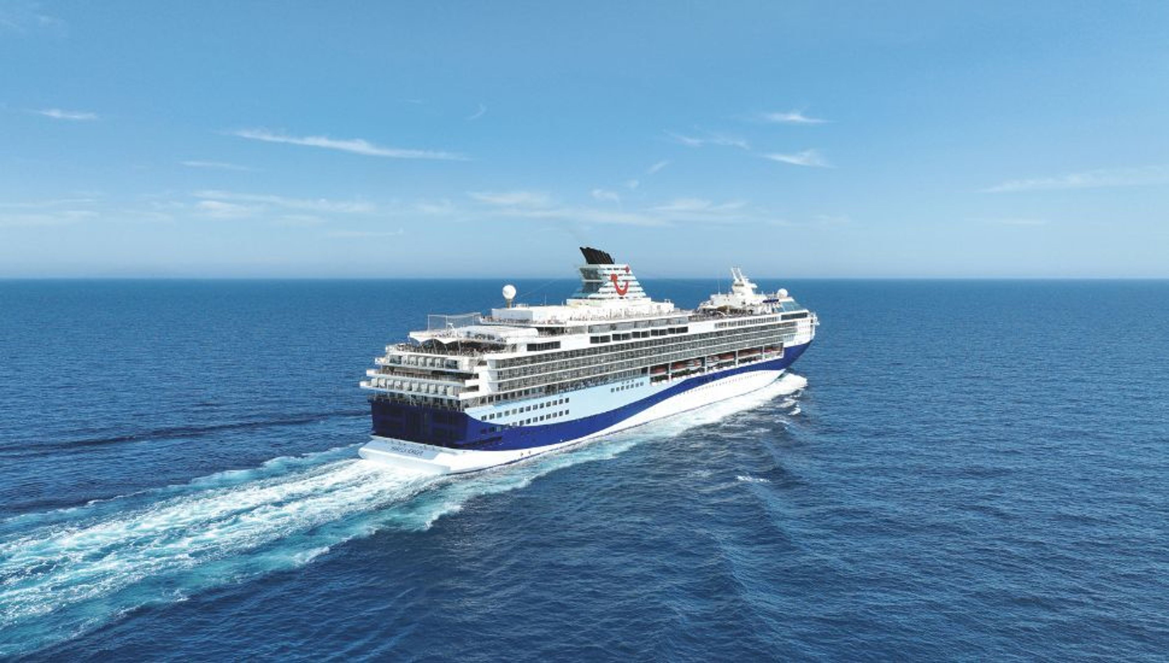 Blue and white cruise ship sailing on the open ocean under a clear blue sky, leaving a white wake.