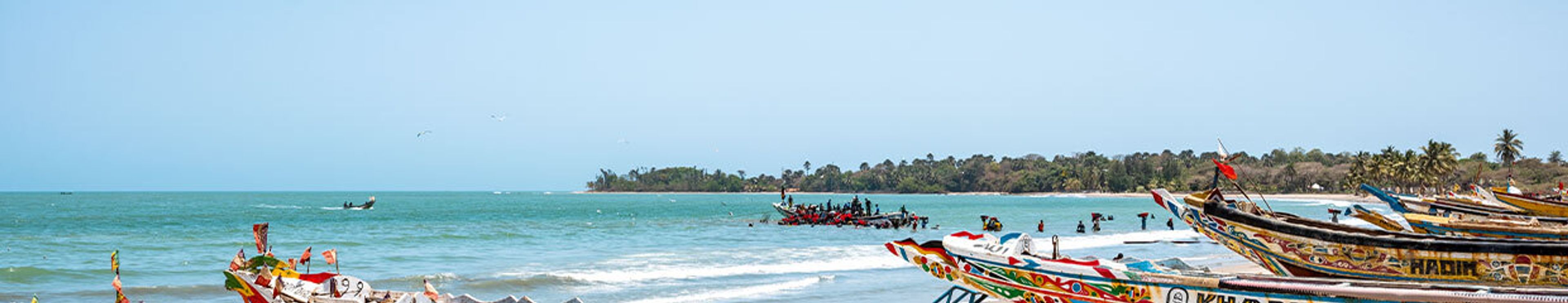 Colorful fishing boats on a sunny beach with turquoise water, people, and palm trees.