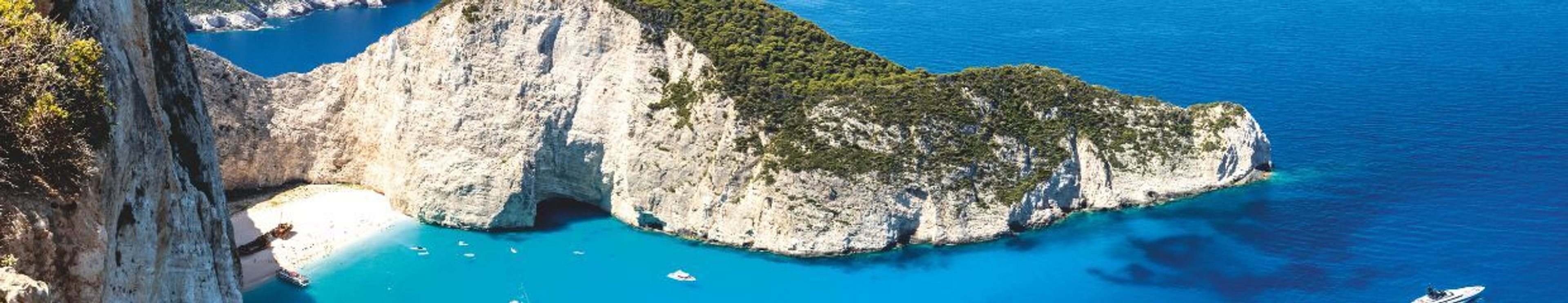 Panoramic view of Navagio Beach in Zakynthos, with a white sandy cove, turquoise water, and steep cliffs.