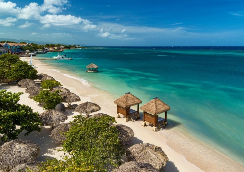 Tropical white sand beach with thatched umbrellas, beachside cabanas, and turquoise water.