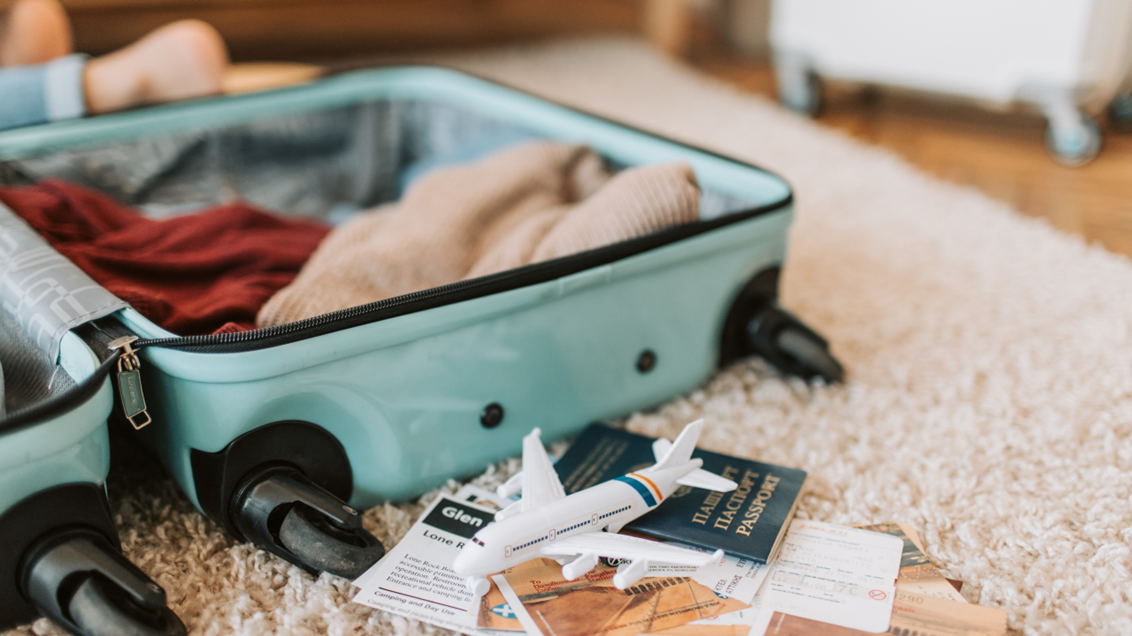 An open light blue suitcase with clothes, a toy airplane, passports, and travel documents on a rug.