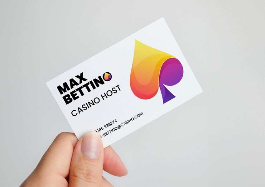 A hand holds a business card for Max Bettino, Casino Host, featuring a colorful spade logo.