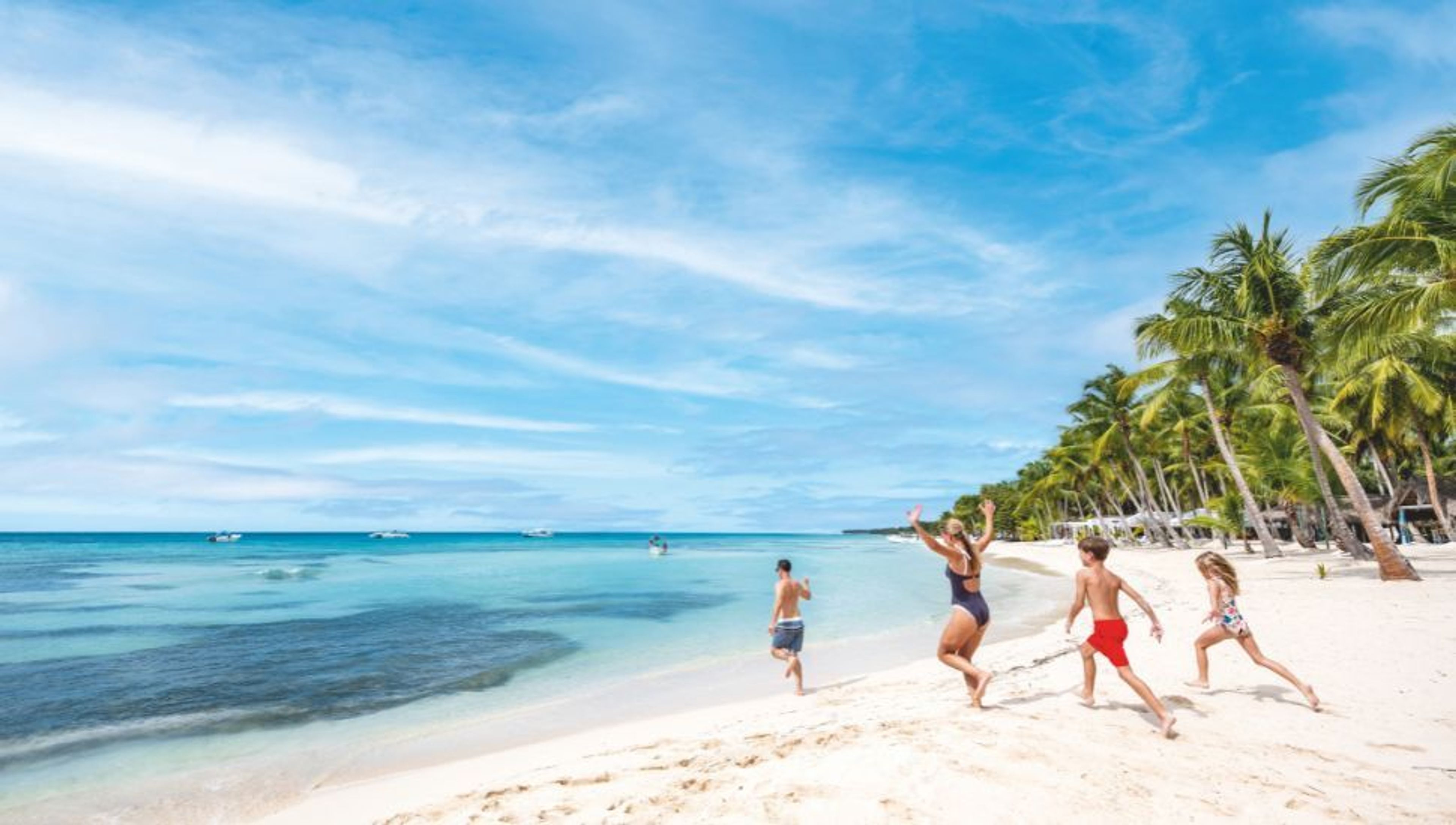A family runs and jumps on a white sand beach with palm trees and clear blue water.