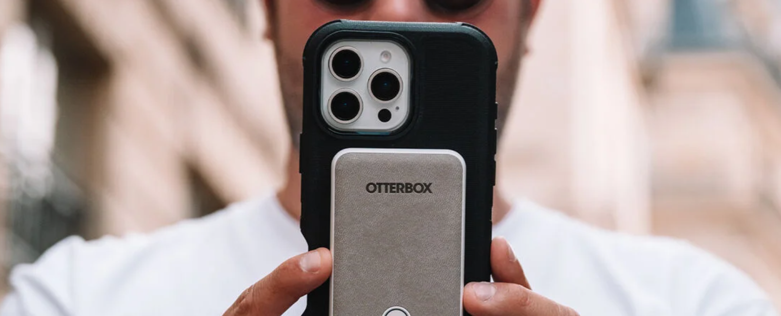 Close-up of a person holding an iPhone in a black case with an OtterBox MagSafe accessory attached.