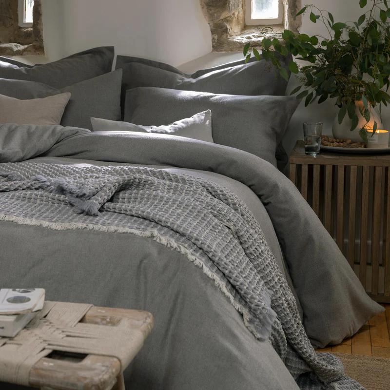 A bed with grey bedding and a textured throw blanket in a rustic room.