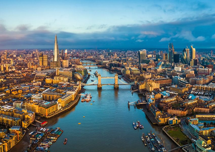 Aerial view of London with the River Thames, Tower Bridge, The Shard, and skyscrapers at sunrise.
