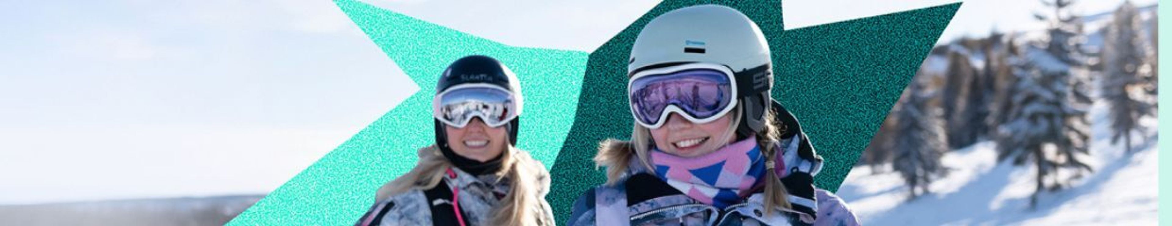 Two smiling women in ski helmets and goggles on a snowy mountain.
