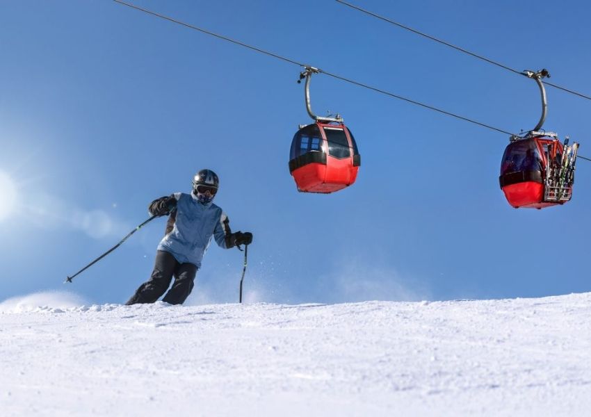 A skier on a snowy slope with two red gondola cabins in the sky.