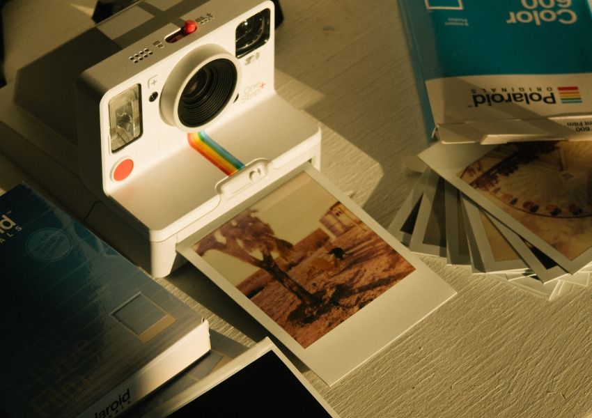 A white Polaroid camera with an instant photo emerging, surrounded by film boxes and developed prints.