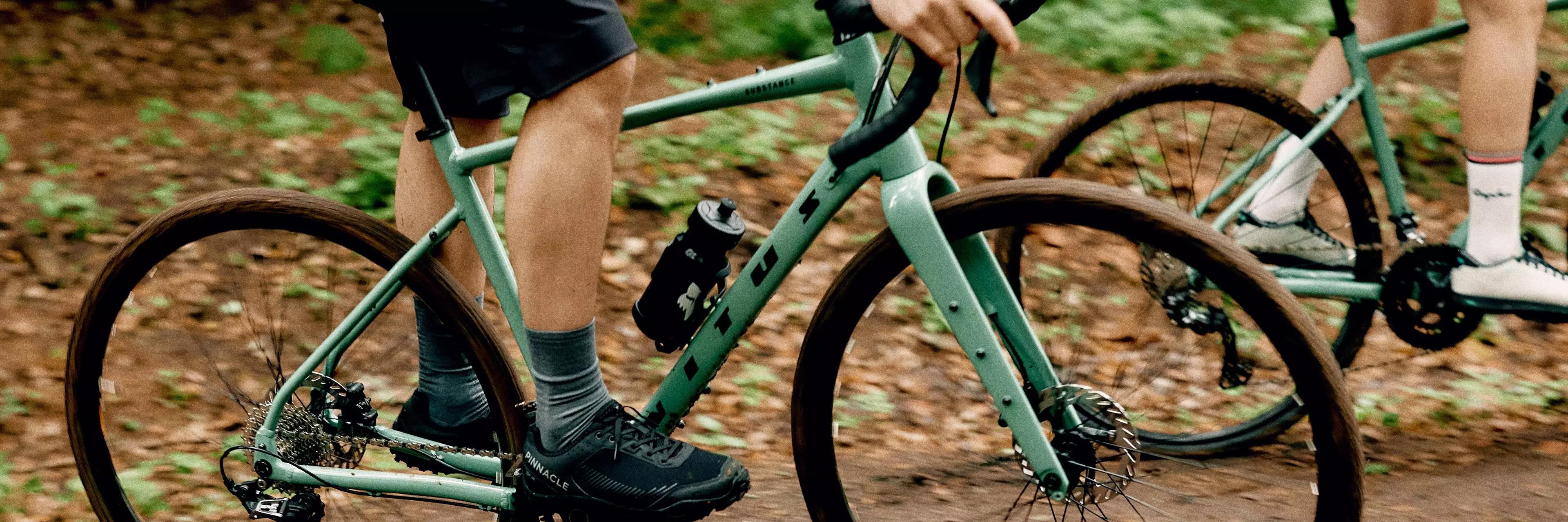 Two people riding green bicycles on a dirt path.