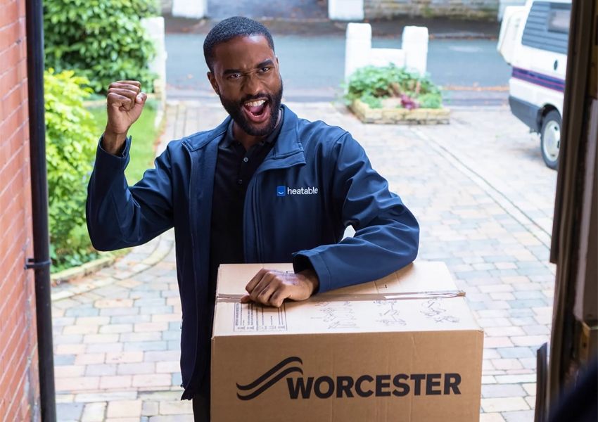 A man in a Heatable uniform enthusiastically delivers a large Worcester box, raising his fist in celebration.