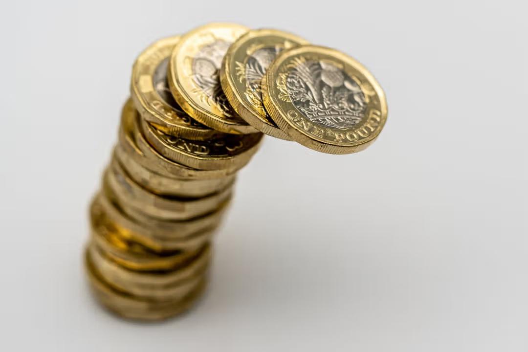 A leaning stack of gold British One Pound coins.