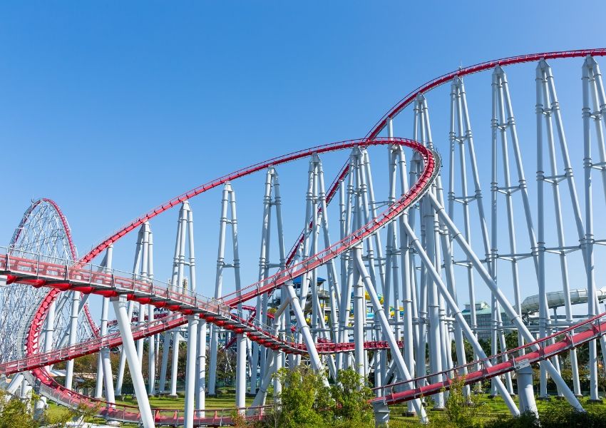 A red and white roller coaster track twists against a clear blue sky.