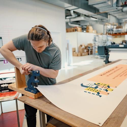 Spir Grafisk, printavdeling. Lærling som monterer maljer på banner.