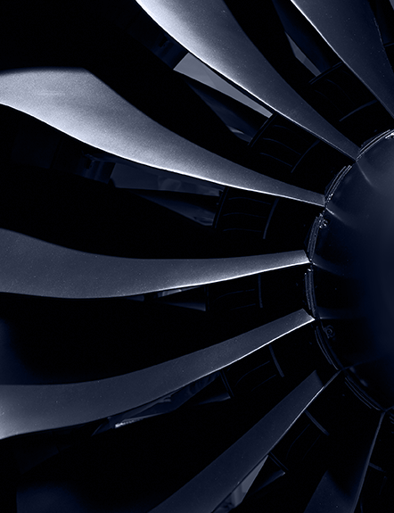 Close-up of a jet engine turbine. Dark, metallic blades curve against a black background.