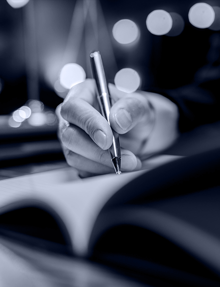 Hand writing in a book with a silver pen, bokeh lights in the background.