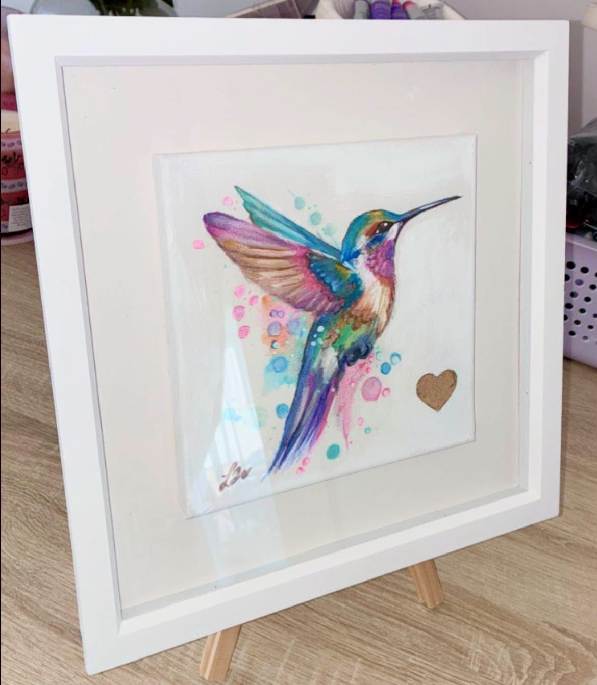 Colourful hummingbird artwork in a white frame, photographed from an angled side view