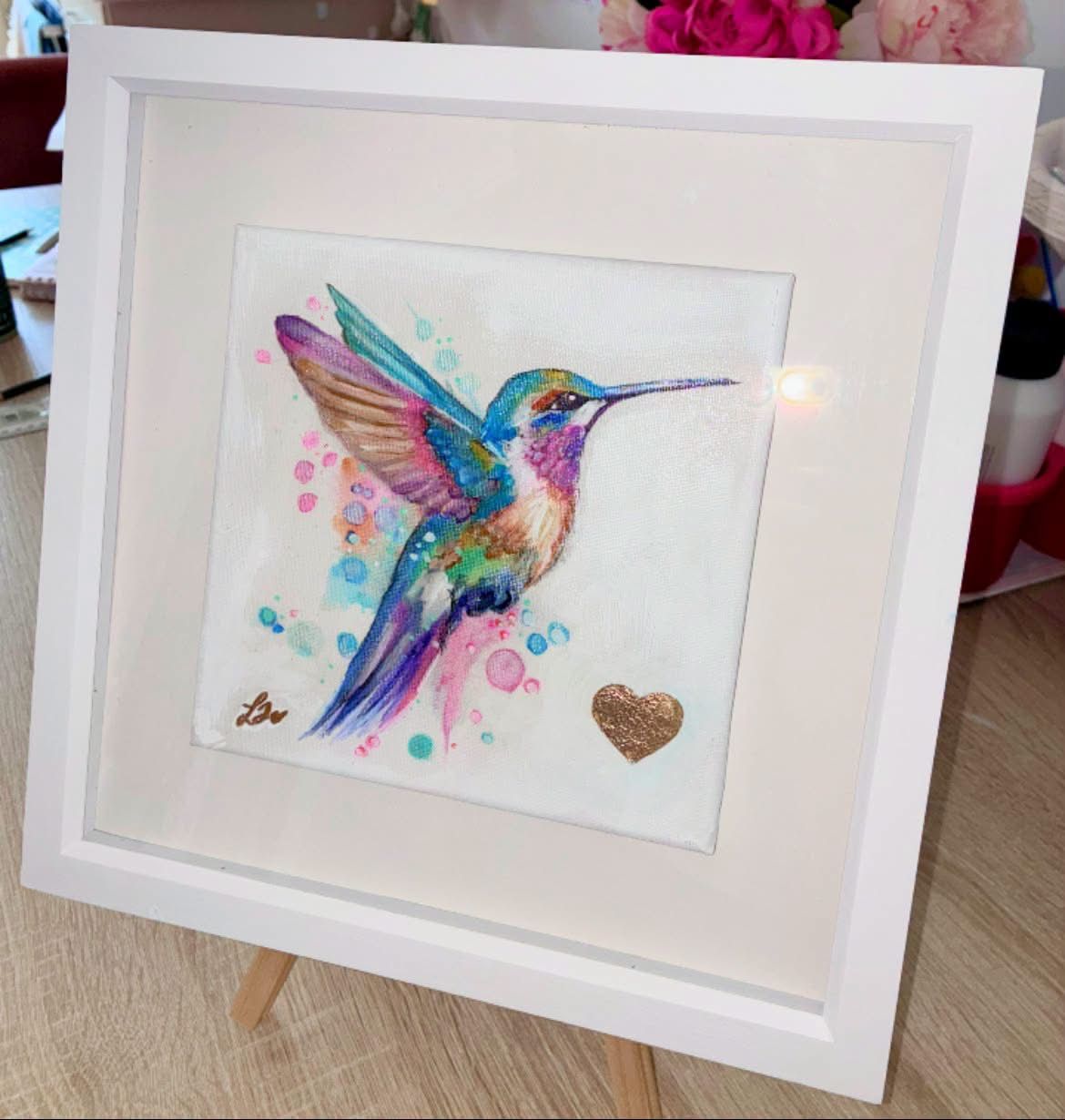 Colourful hummingbird artwork in a white frame, photographed from another angled view