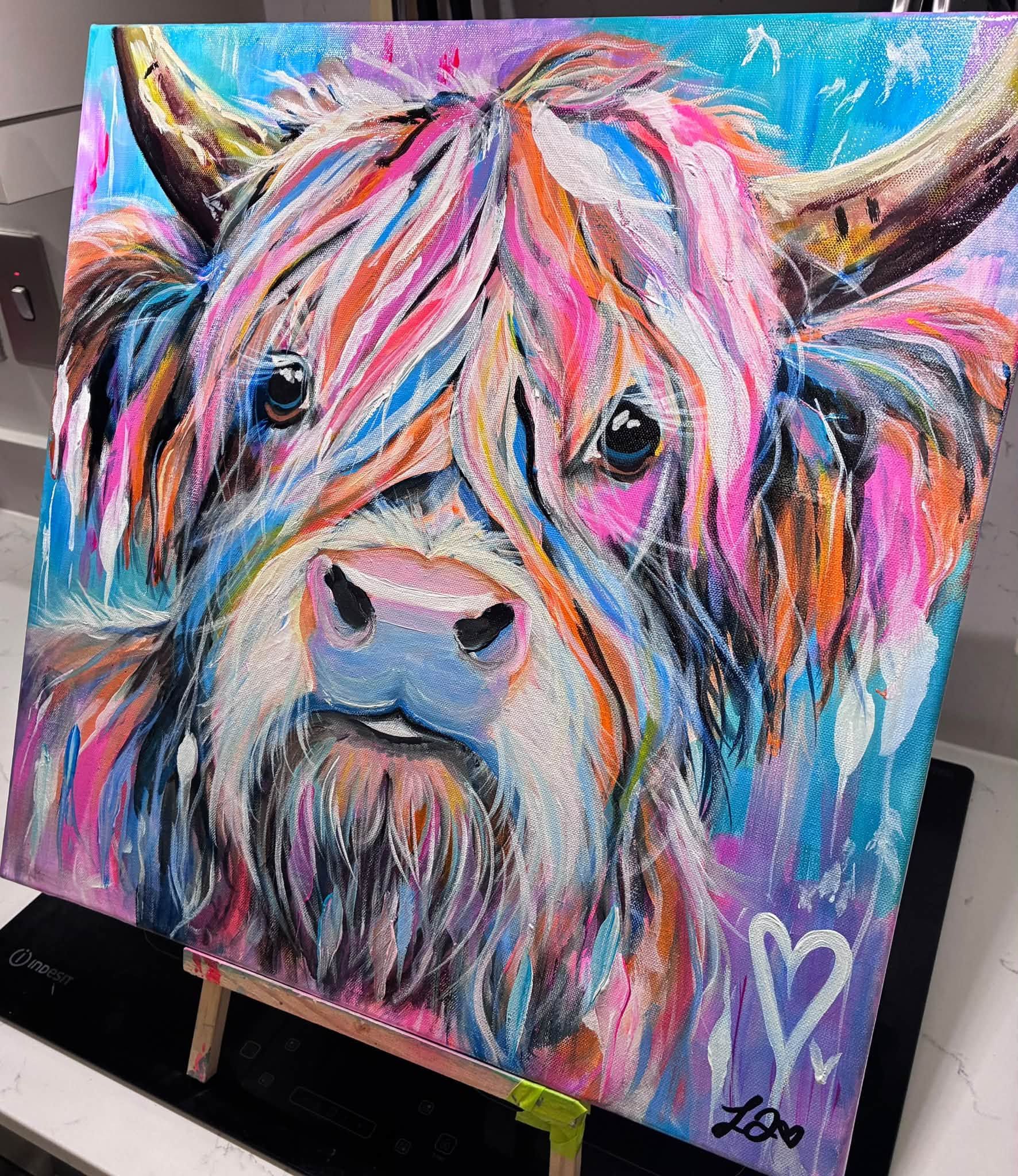 Angus Has Notions acrylic painting displayed on an easel, showing a colourful highland cow with flowers around its horns