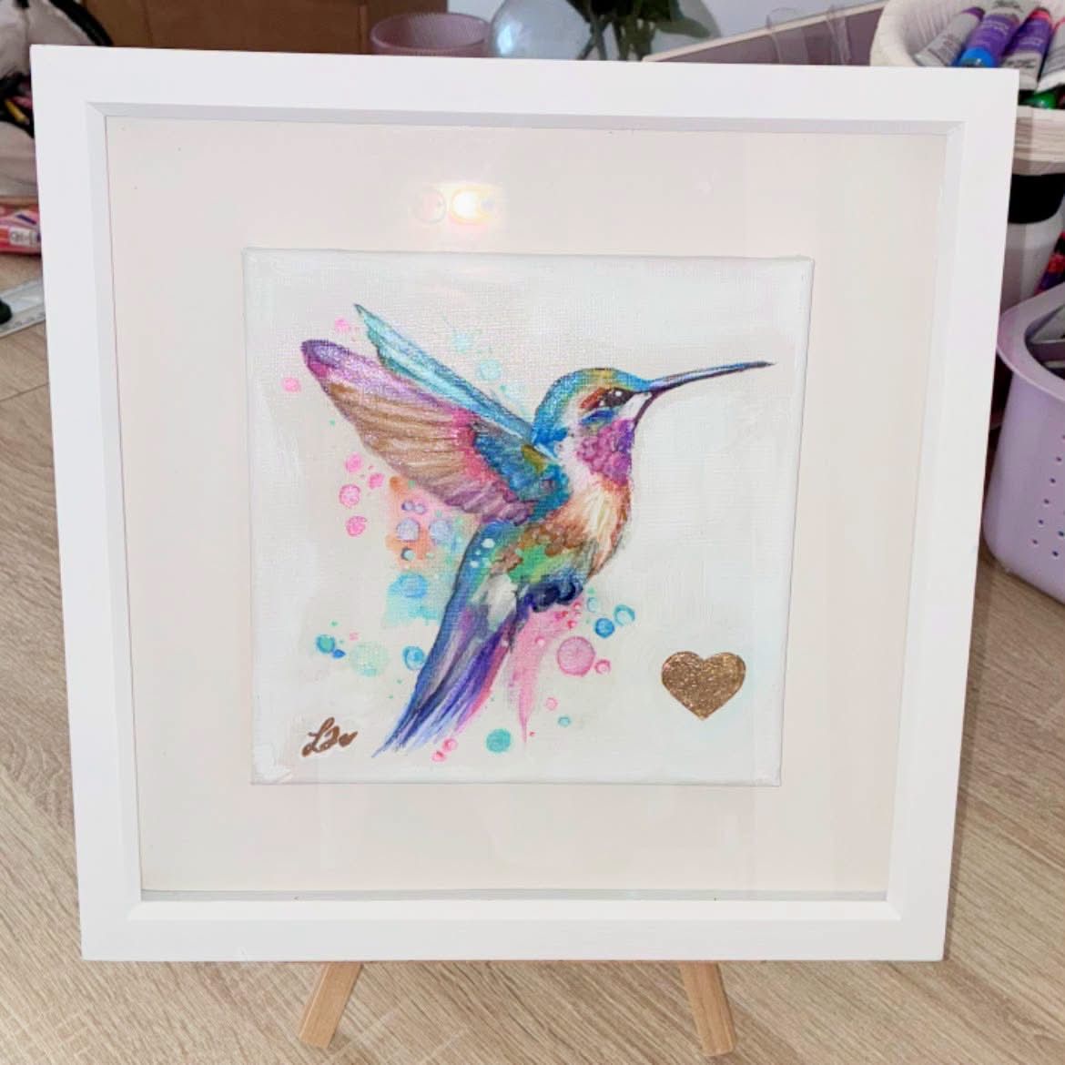 Colourful hummingbird artwork in blue, turquoise, pink and gold, displayed in a white frame