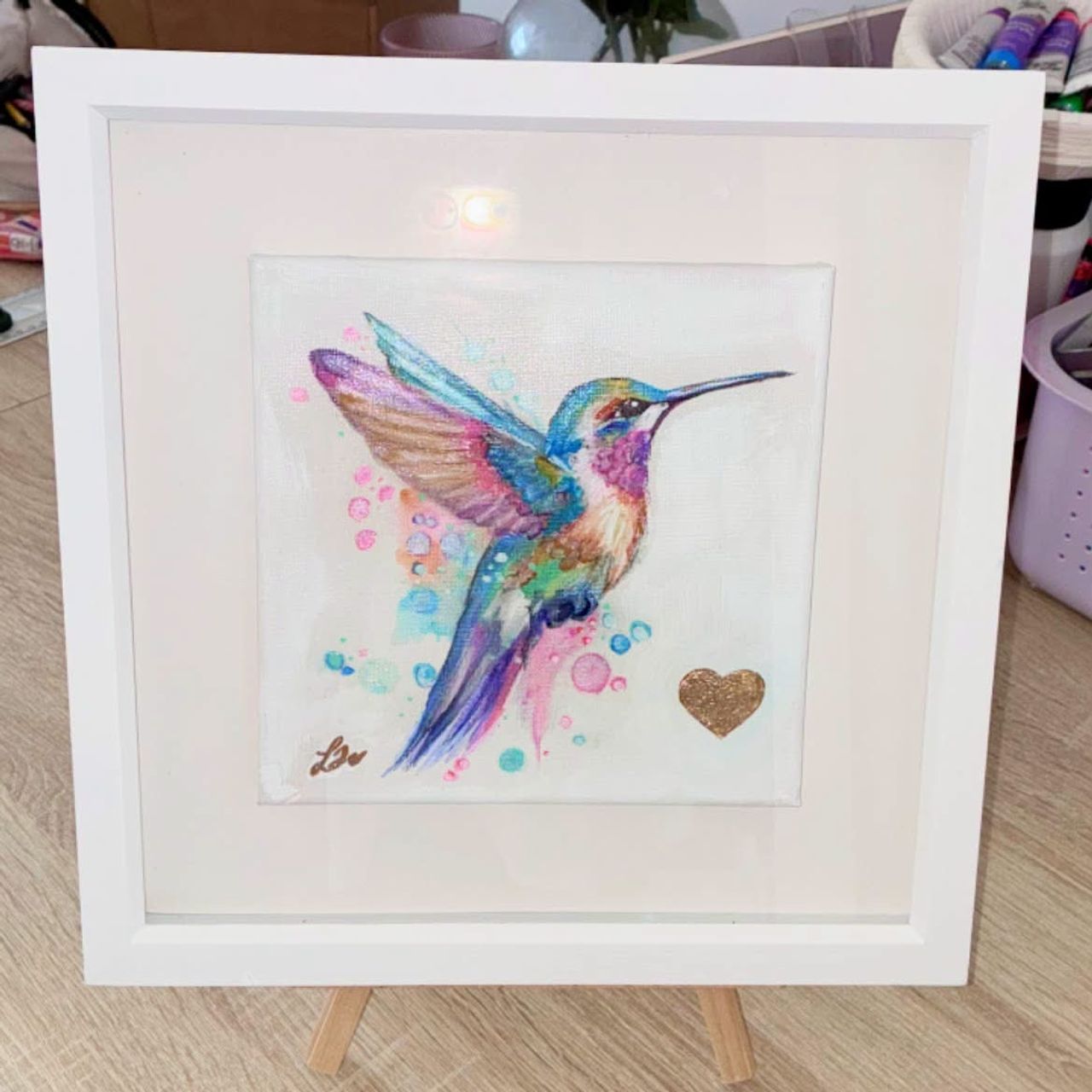 Colourful hummingbird artwork in blue, turquoise, pink and gold, displayed in a white frame