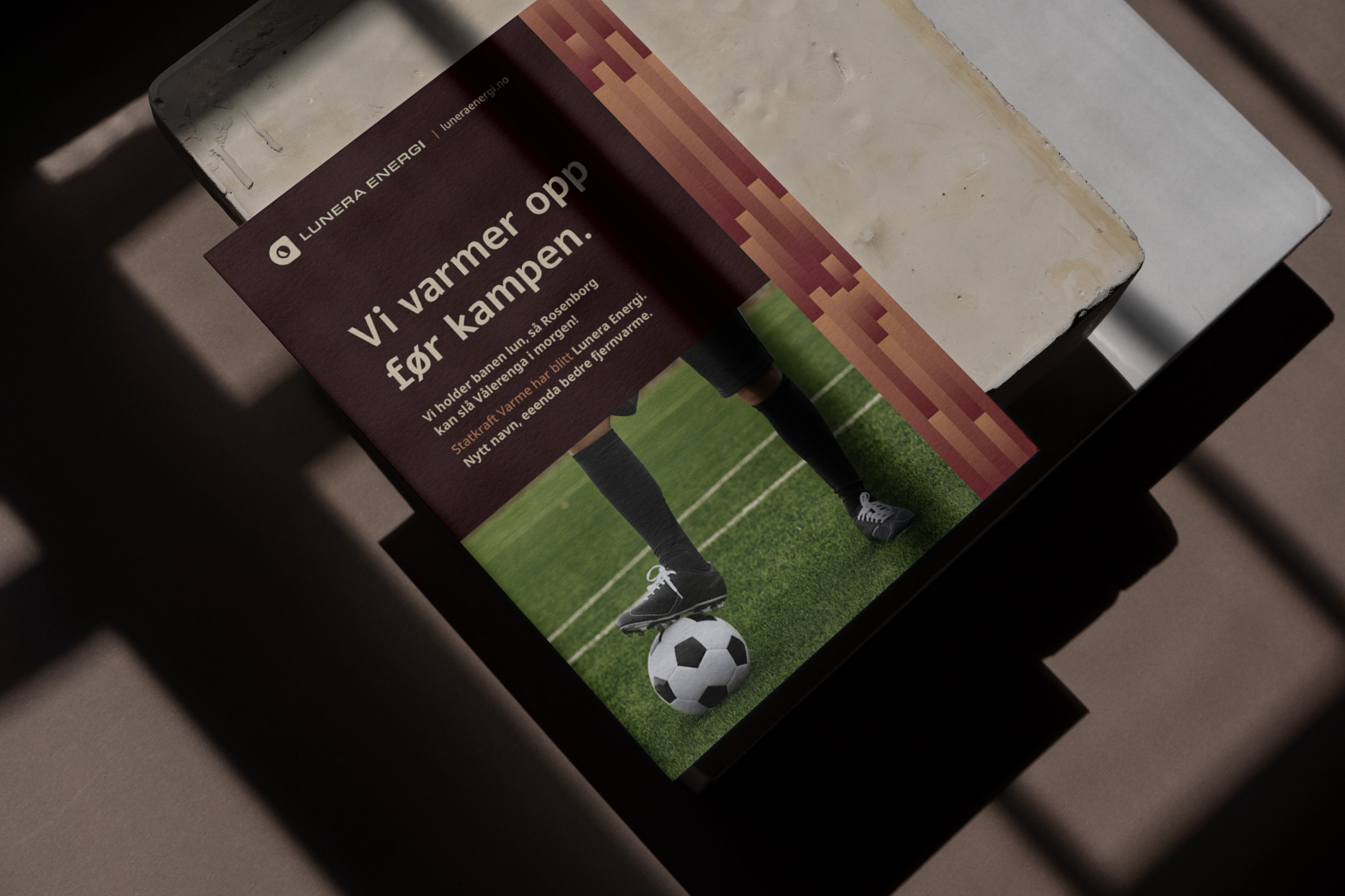 Plakat i sollys på en benk: «Vi varmer opp før kampen», med en fotballspiller som holder foten på ballen på kunstgress.