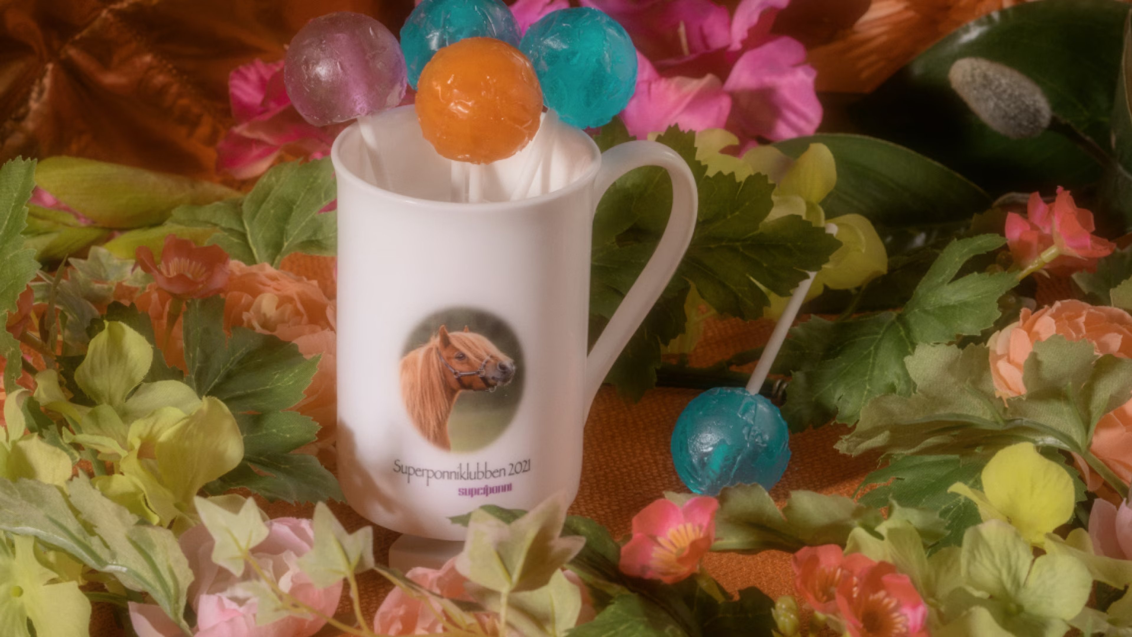Krus med ponnimotiv blant blomster og fargerike kuler