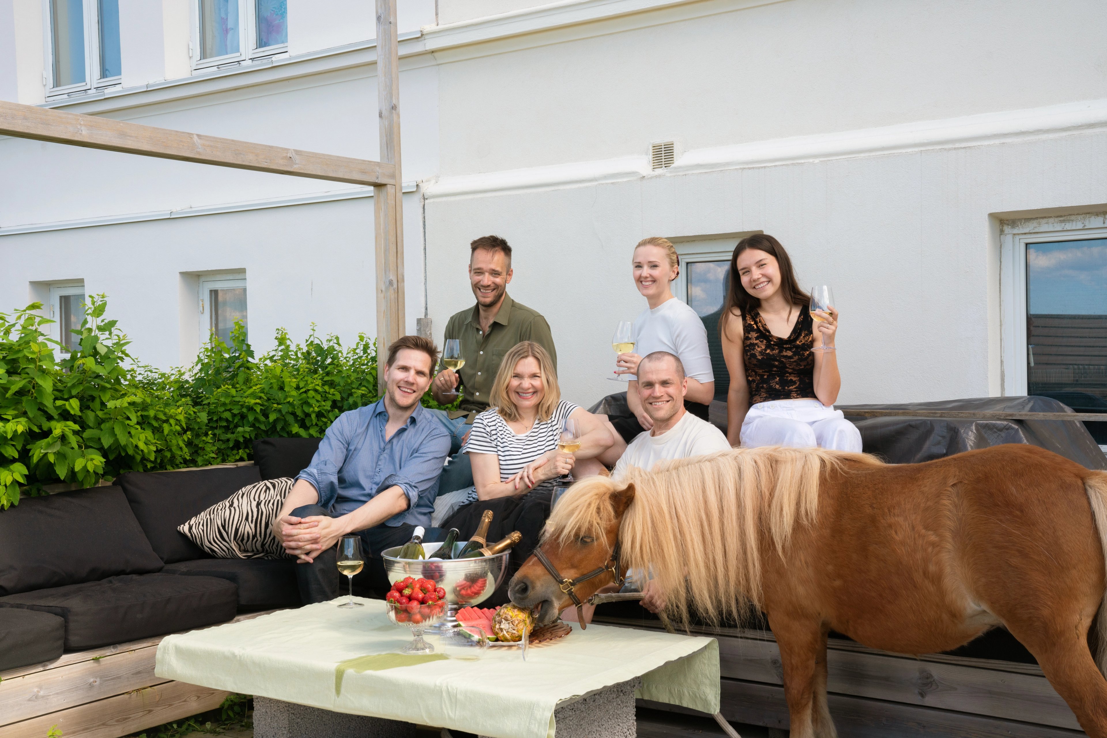 Gjengen i en sofa på en terrasse med glass i hendene, og en ponni som forsyner seg av jordbærene på bordet