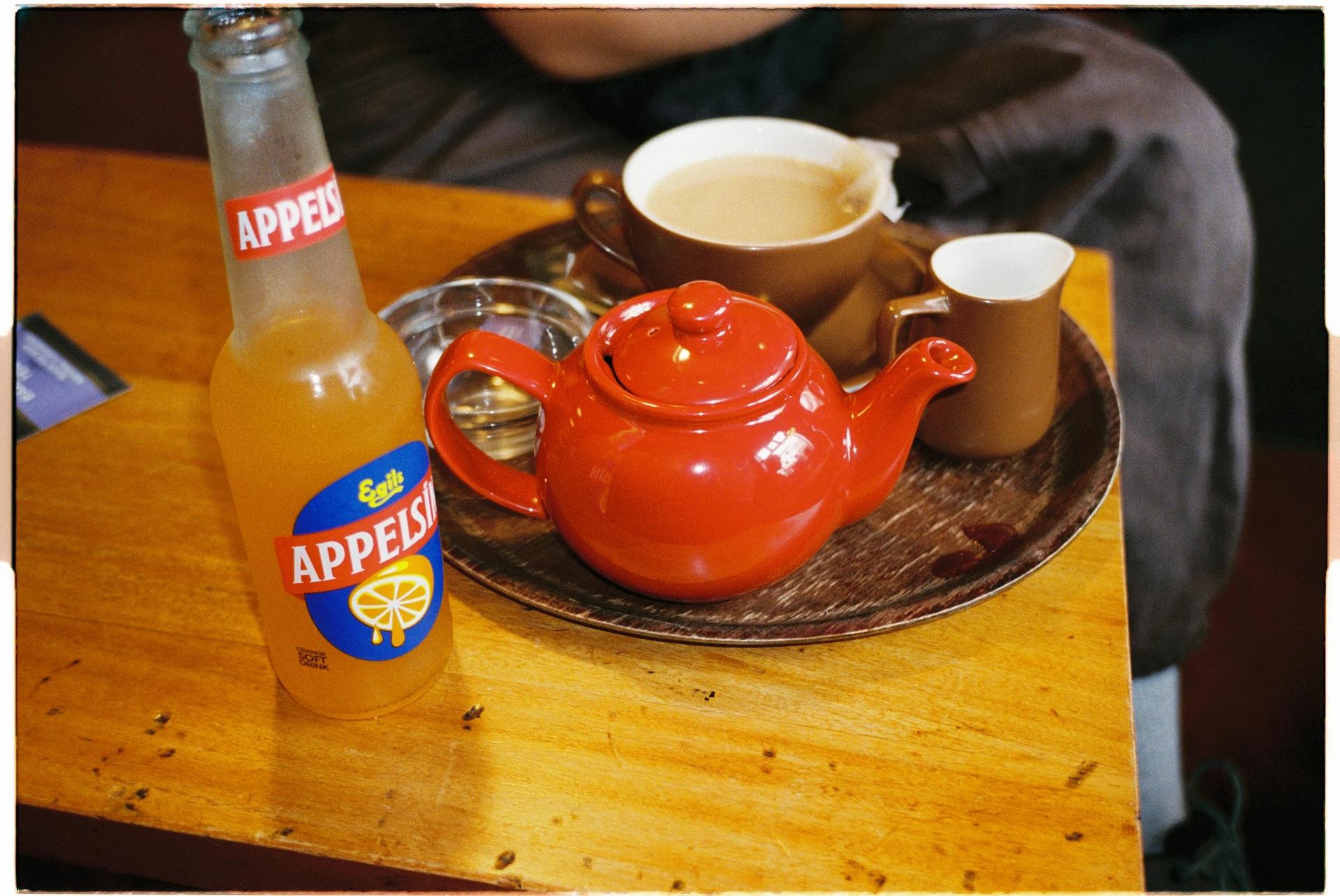 En rød tekanne, kopper og en flaske Appelsin på et trebord